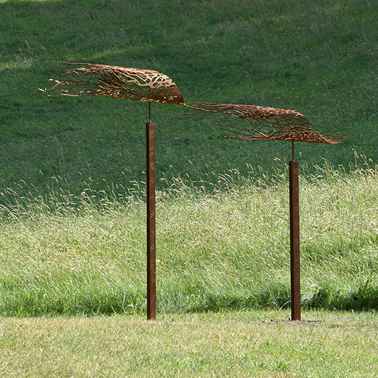 Twee cortenstalen beelden, op cortenstalen sokkels, die als vanen lijken te wapperen in de wind met organische uitsparingen die geïnspireerd zijn op de zee.