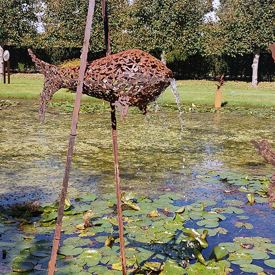 Visvormig beeld tussen twee palen van cortenstaal, geplaatst in een vijver.